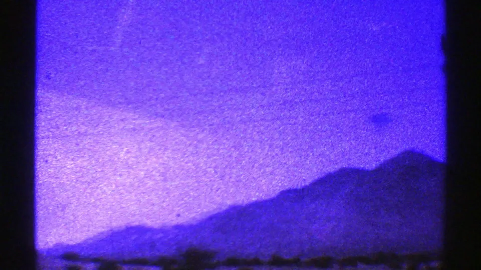 Nevada 1969 home-movie frame showing a distant mountain ridge under an intensely blue-purple sky.