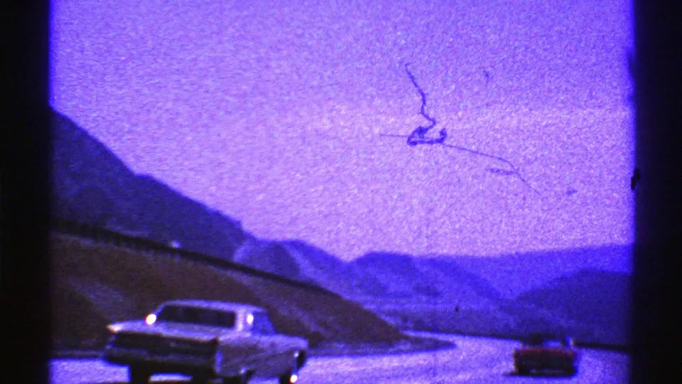 Nevada 1969 road-trip frame with classic cars on a winding highway through blue-tinted mountain scenery.