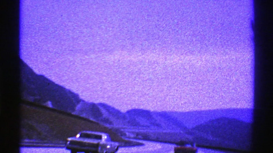 Nevada 1969 8mm frame of classic cars on a mountain highway, filmed from a moving road-trip perspective.