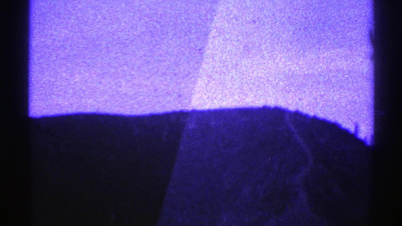 Purple-tinted view through a moving vehicle toward a mountain road and dark frame edges.