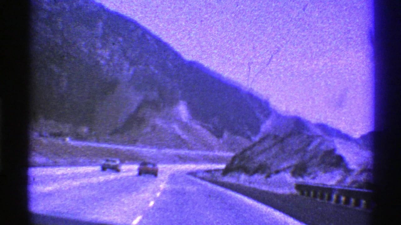 1969 Nevada 8mm frame showing a highway through a mountain pass, filmed from inside a moving vehicle with cars and guardrail visible.
