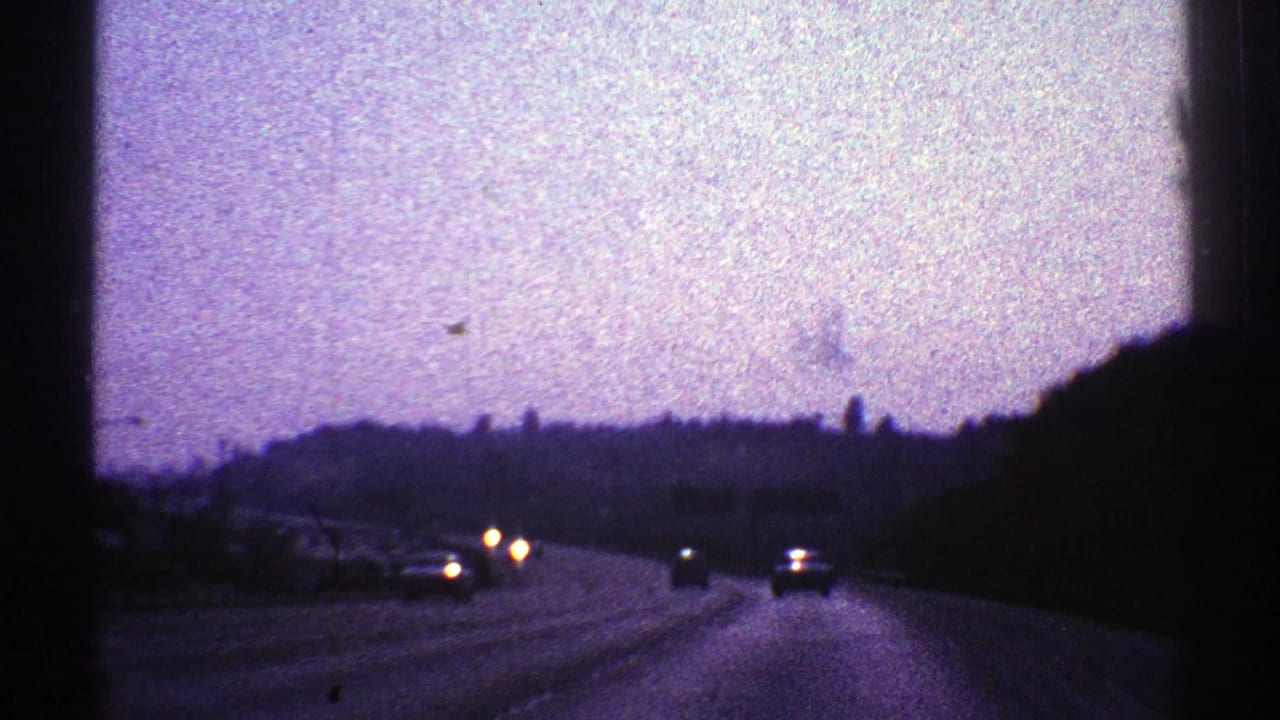 1969 Nevada road scene at dusk, with car headlights on a major highway and low hills silhouetted in the distance.
