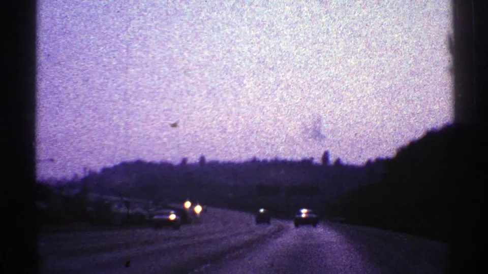 1969 Nevada road scene at dusk, with car headlights on a major highway and low hills silhouetted in the distance.
