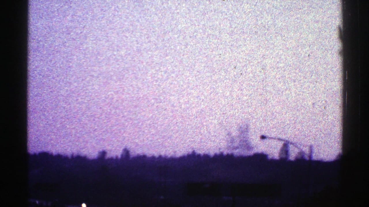 1969 Nevada 8mm frame showing a dark skyline or roadside silhouette beneath a grainy purple sky, with a streetlight arm visible.