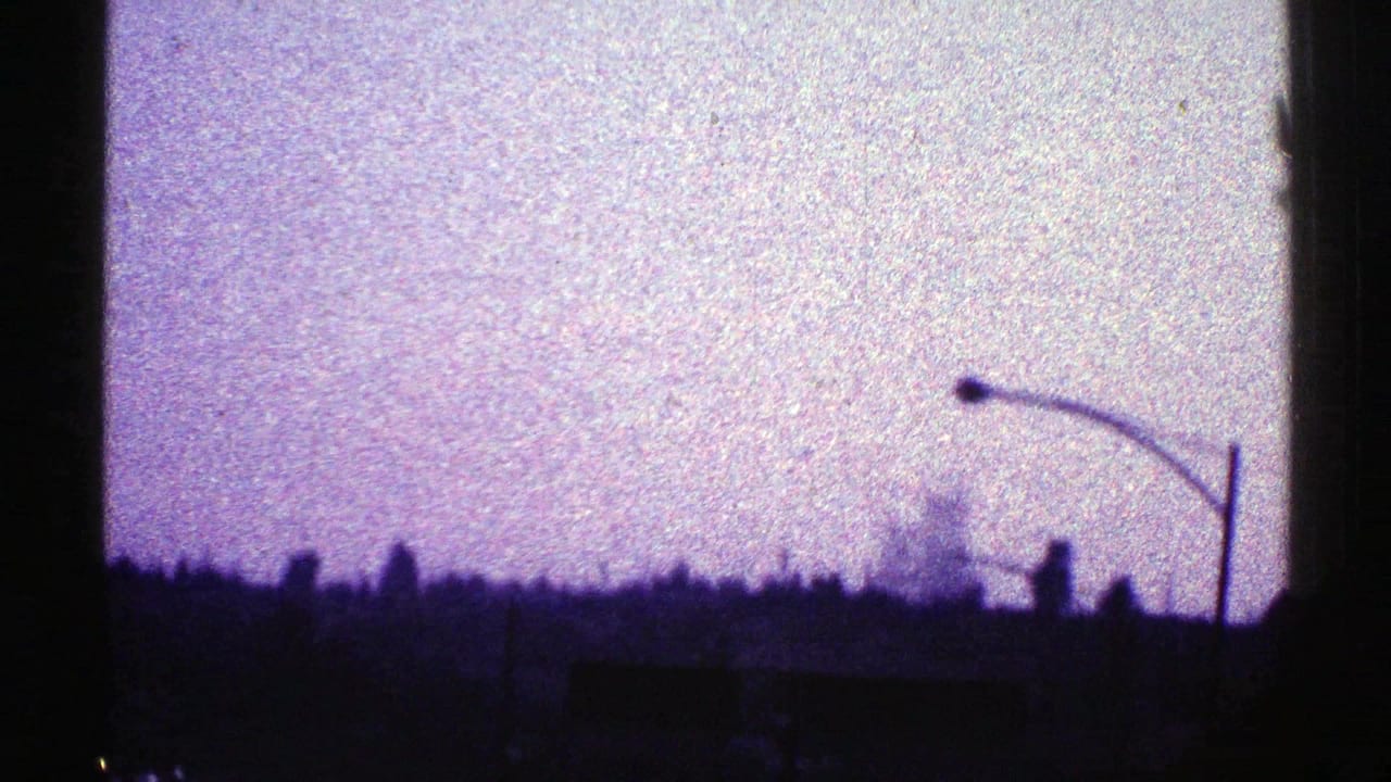 1969 Nevada home-movie frame with a streetlight, low urban silhouettes, and a bright purple-shifted sky at dusk.