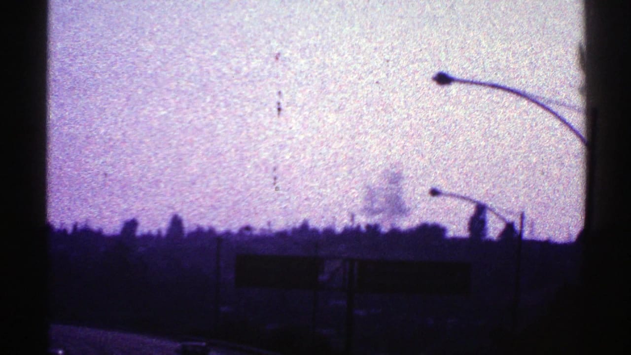 Purple sky above a dark roadside horizon with streetlights and partial highway signs.