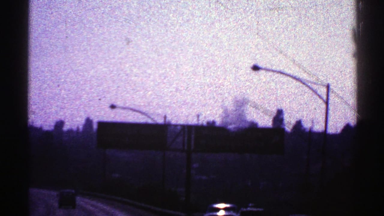 1969 Nevada highway view with dark overhead signs, curved streetlights, distant trees, and a car light near the bottom edge.