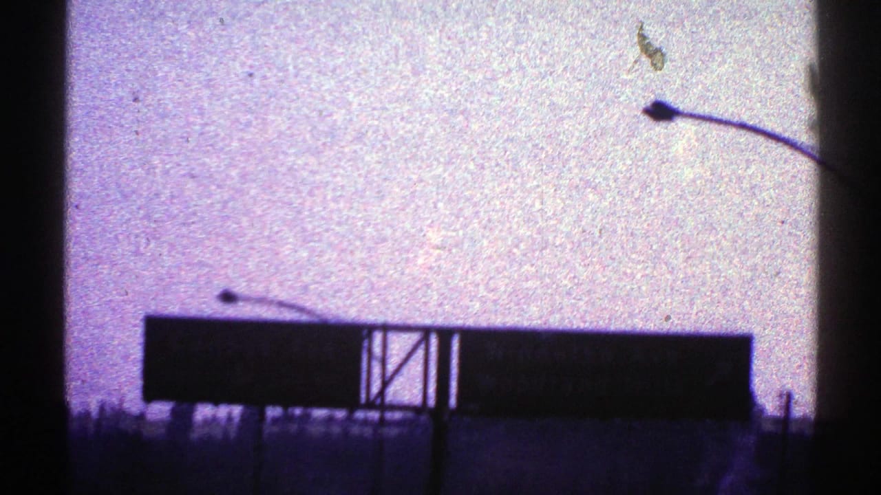 1969 Nevada 8mm frame with a large silhouetted highway sign, streetlight arm, roadside posts, and grainy purple sky.