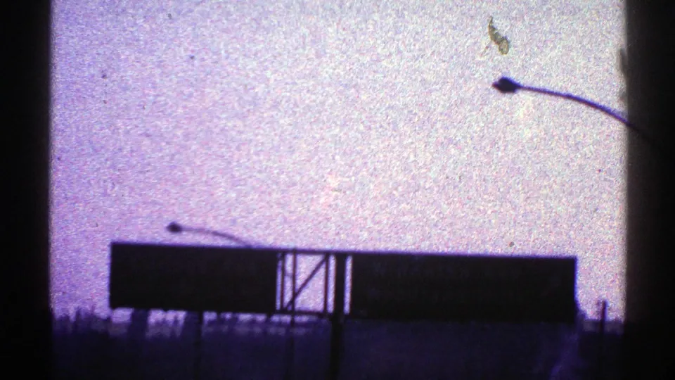 1969 Nevada 8mm frame with a large silhouetted highway sign, streetlight arm, roadside posts, and grainy purple sky.
