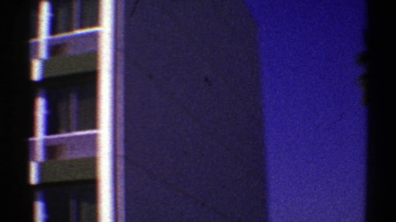 1969 Nevada 8mm frame with a partial modernist building facade, vertical column, and palm fronds under a deep blue sky.