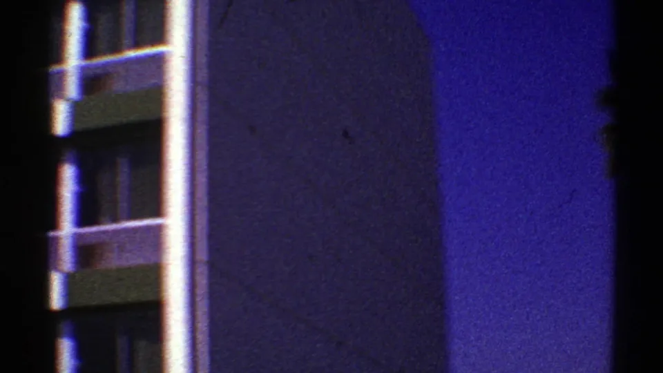 1969 Nevada 8mm frame with a partial modernist building facade, vertical column, and palm fronds under a deep blue sky.