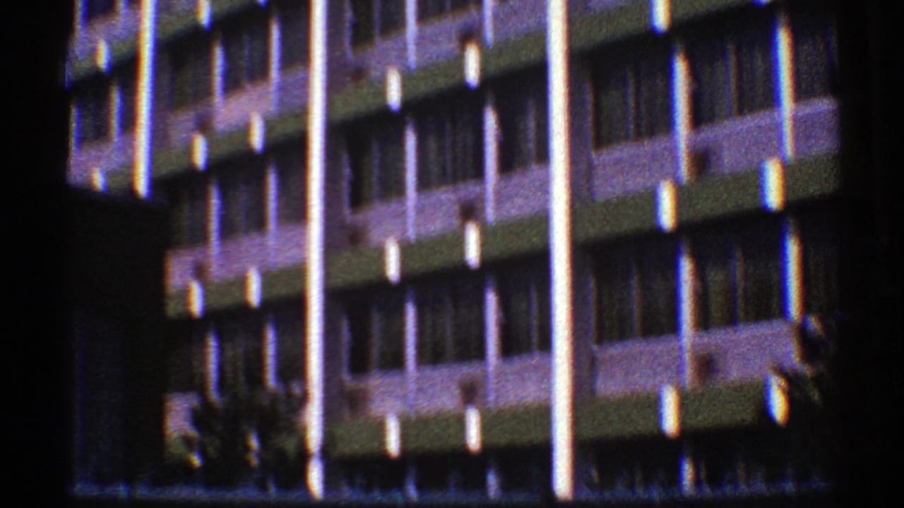1969 Nevada 8mm frame showing a wider view of a modernist building facade with repeated window bays and small palms near the base.