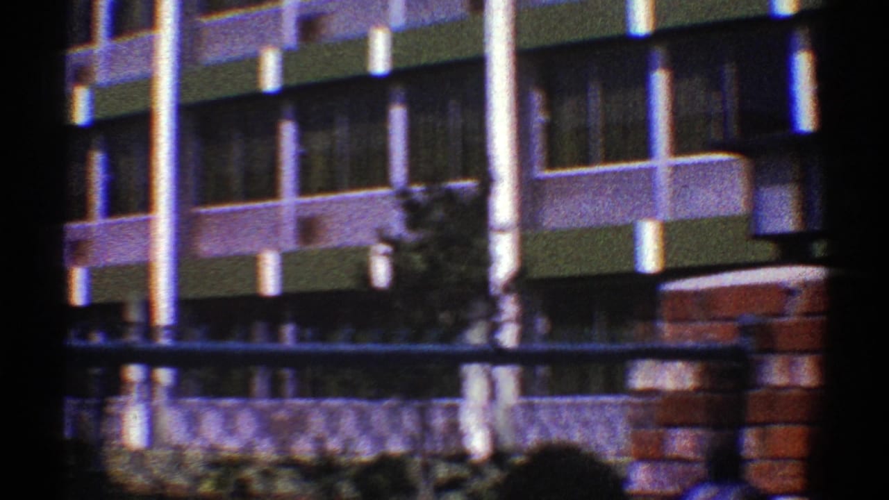 1969 Nevada 8mm view of a green and white building exterior seen past chain-link fencing and brick gate pillars.