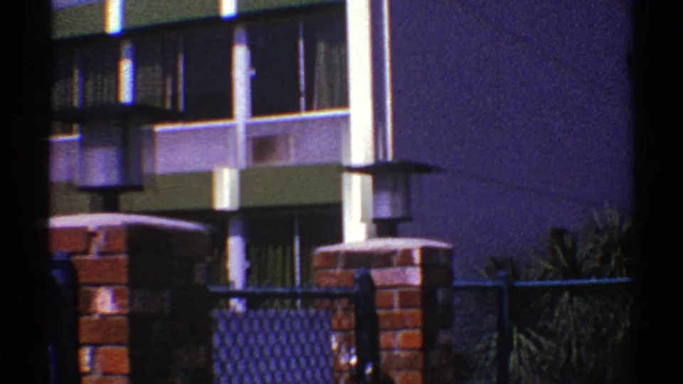 1969 Nevada 8mm frame showing windows and green facade panels with a brick pillar and outdoor lamp in the foreground.