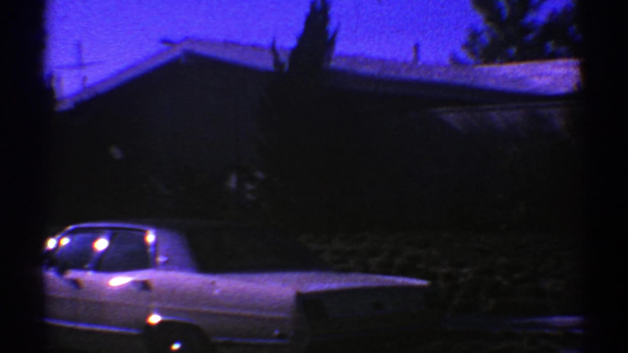 1969 Nevada 8mm frame showing a classic car parked near a low suburban home under a purple-blue dusk sky.