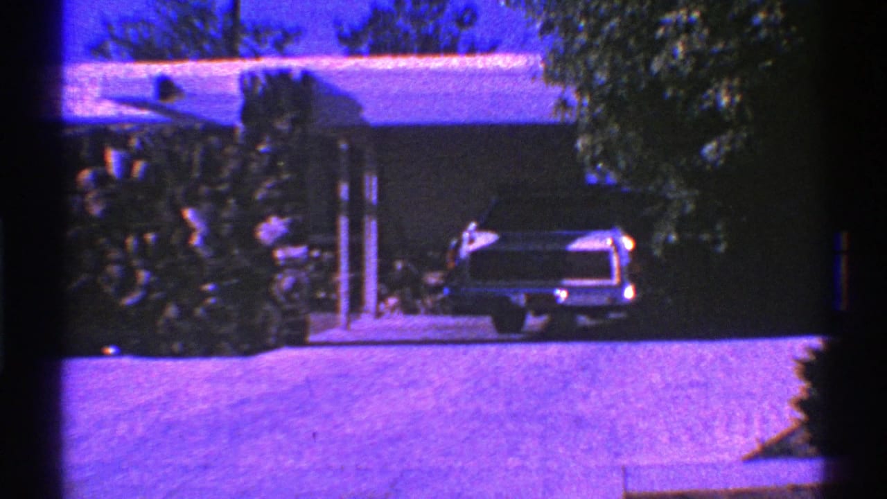 Classic car parked near a house entrance and landscaping.
