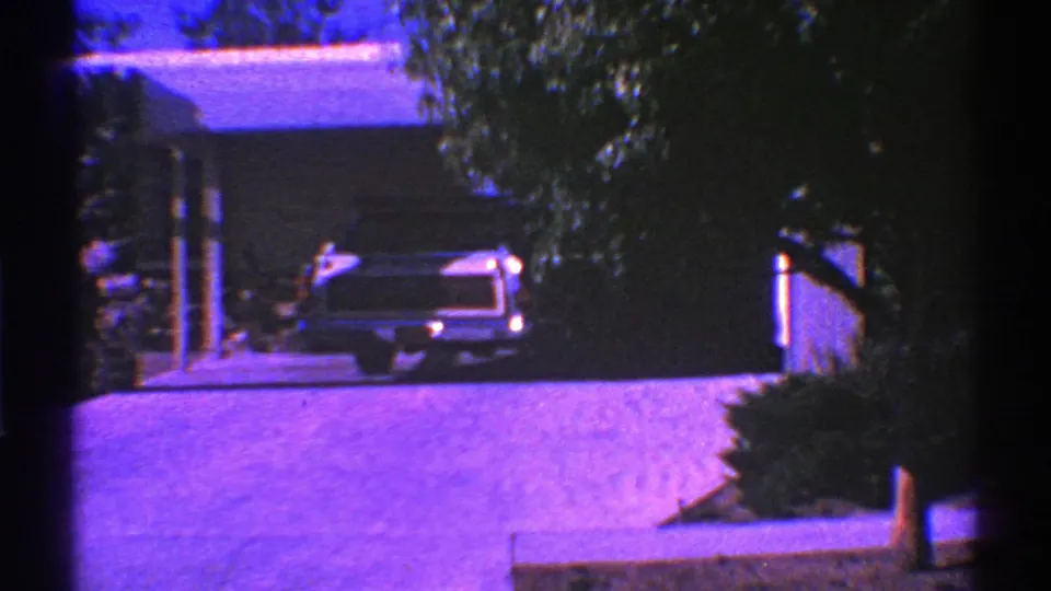 1969 Nevada suburban driveway view with a parked car, single-story house, tree trunk, shrubs, and strong purple film color shift.