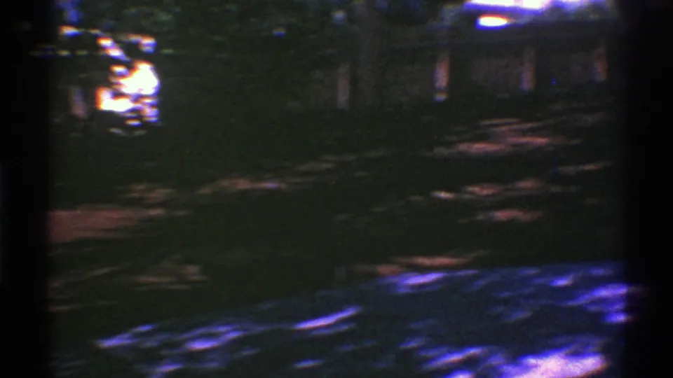 Grainy 1969 Nevada home-movie frame looking over a shaded yard toward trees and a dark fence or exterior structure.