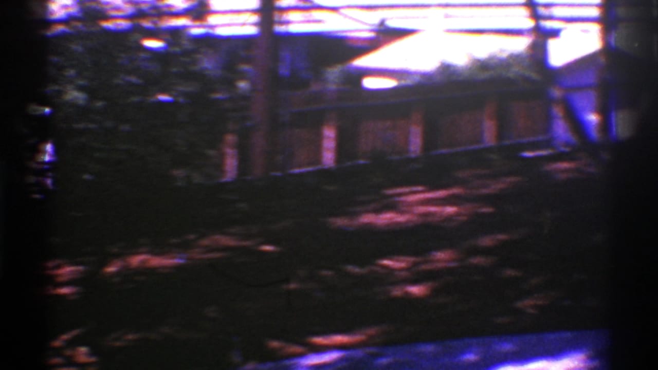 1969 Nevada frame with a red wooden deck behind a shaded yard, plants, and vertical posts.