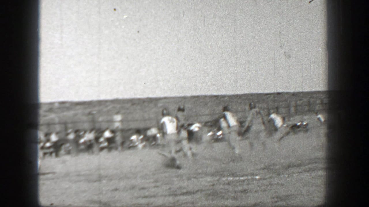 Players run across the field near a sideline with spectators or teammates in the background.