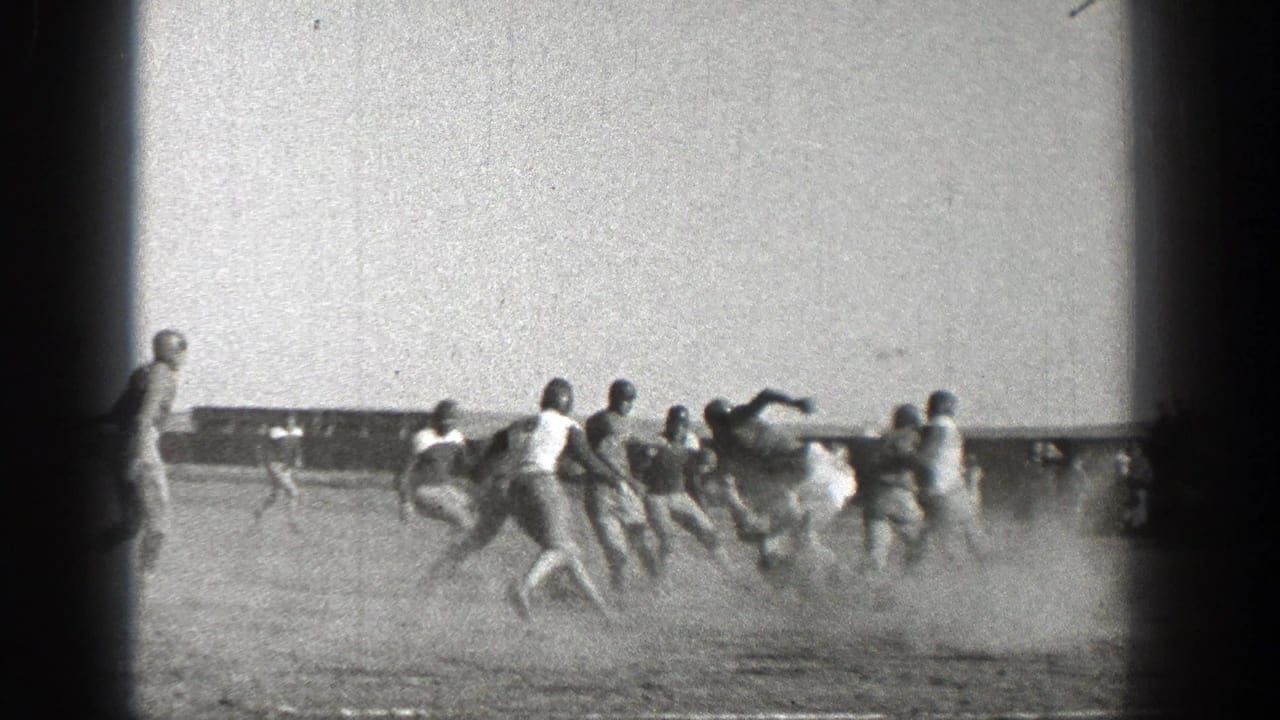 Football players run across a dusty field during a play.