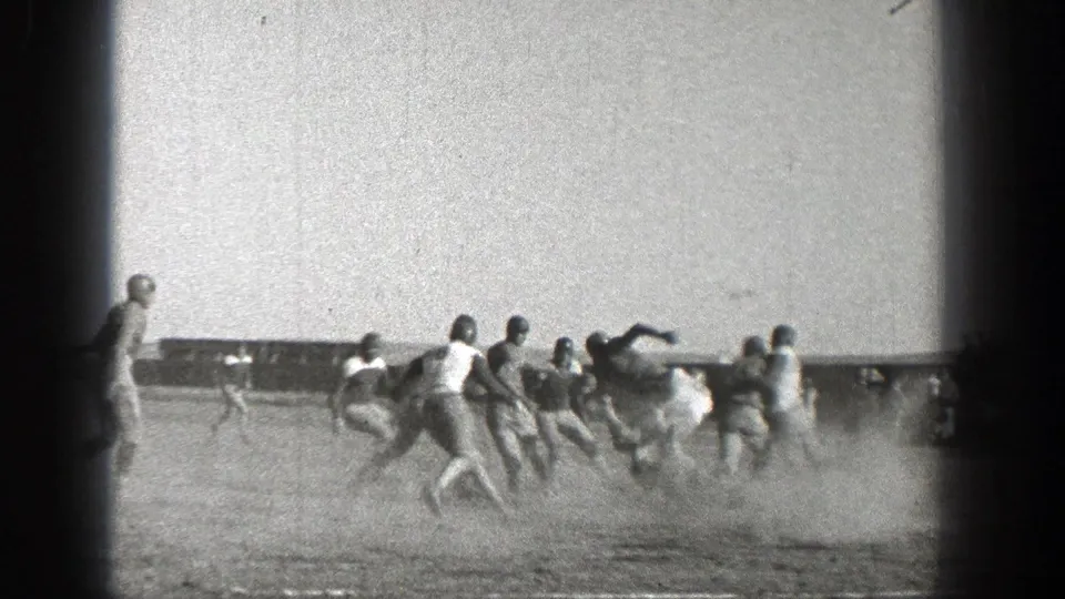 Washington 1938 home-movie frame showing football players in early uniforms running across a dusty outdoor field.