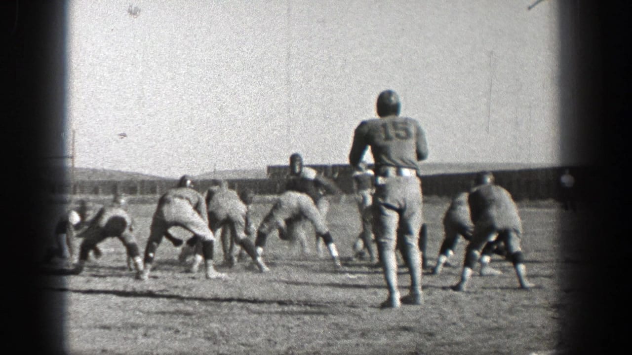 Washington 1938 home-movie frame showing football players in helmets lining up on a grass field before play begins.