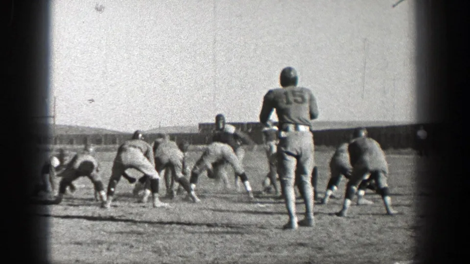 Washington 1938 home-movie frame showing football players in helmets lining up on a grass field before play begins.