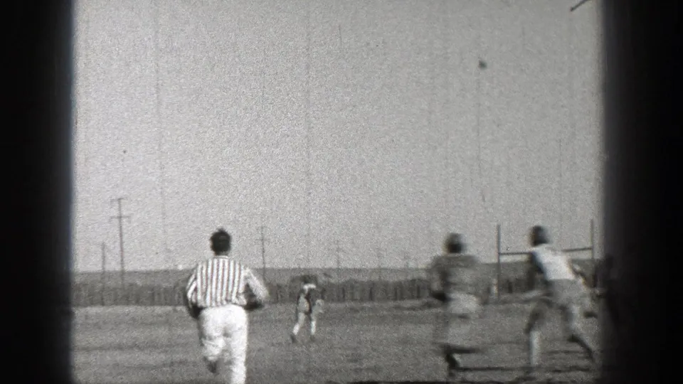 Washington 1938 frame showing a referee in stripes following football players during play on an outdoor field.