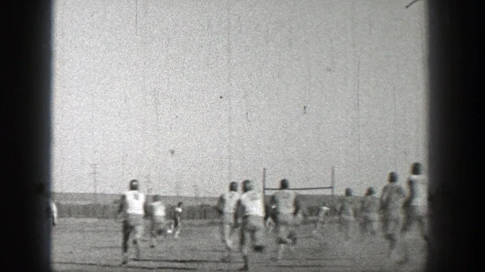 Washington 1938 home-movie frame of football players running across a bright open field near goalposts.