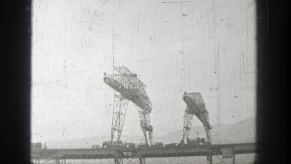 1938 Washington 8mm frame showing two large cranes working near a railroad bridge span in a hazy outdoor view.