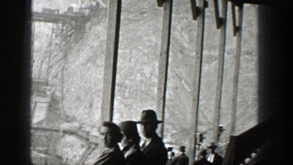 Onlookers in 1938 Washington, including a man in a wide-brim hat, stand beside bridge railings and watch the construction area.