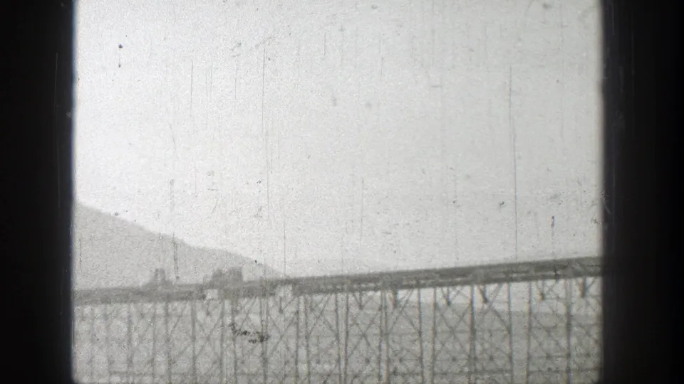 Distant 1938 Washington bridge view with rail cars on the span, lattice supports below, and hazy hills in the background.
