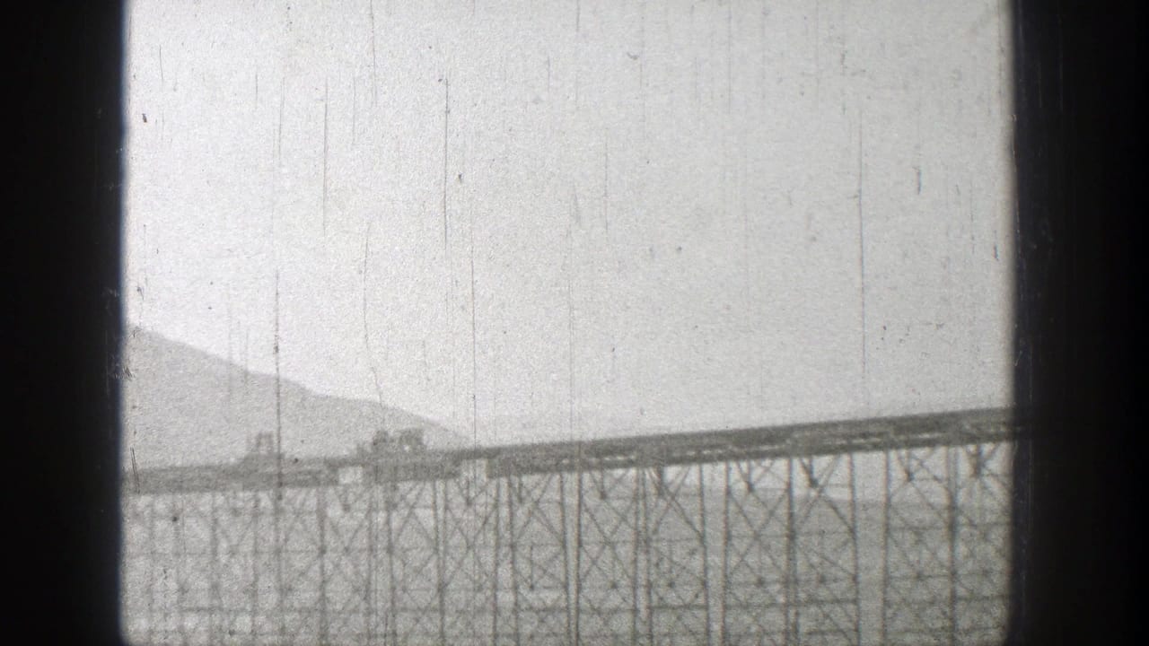 Distant truss rail bridge crossing water with mountains behind it.
