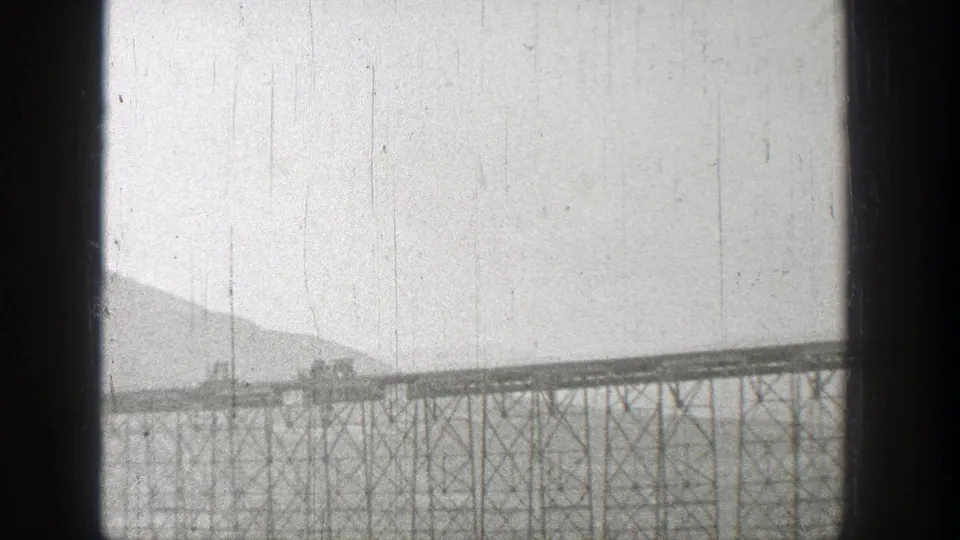 1938 Washington home-movie frame showing a long truss rail bridge over water, with low mountains in the background.
