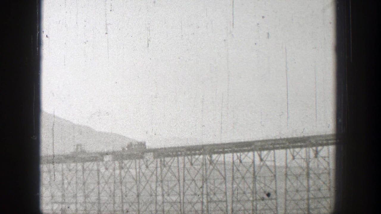 Small train crossing a long truss bridge over water.