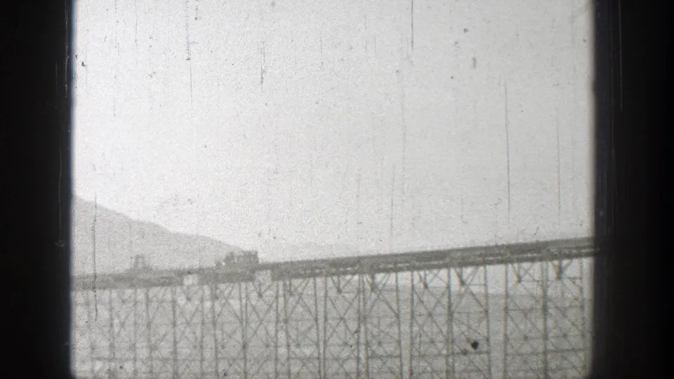 1938 Washington frame with a small train moving along a high truss bridge above a wide body of water.