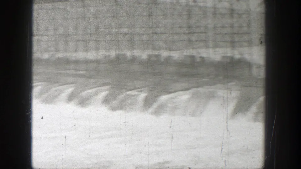 Late-1930s Washington frame showing water cascading over dam spillways below a long steel bridge.