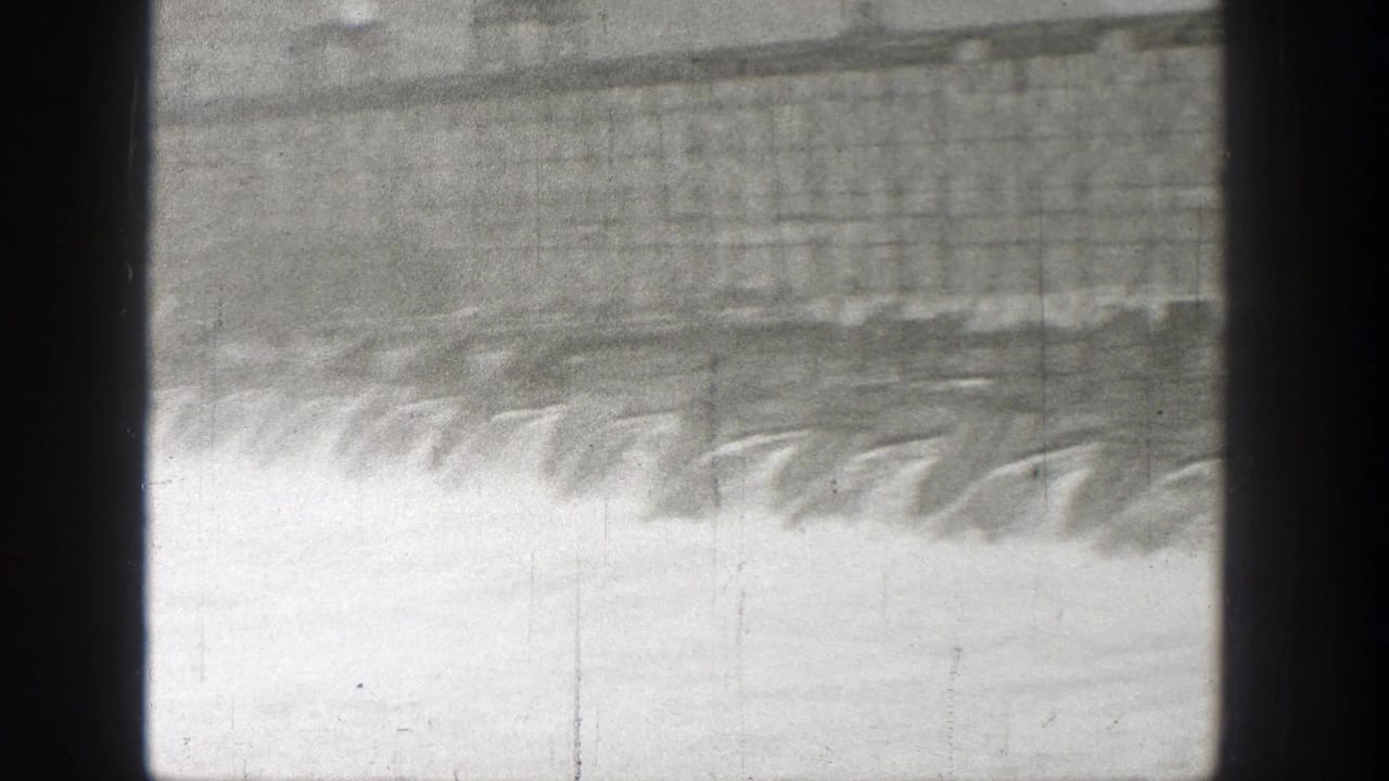 1938 Washington home-movie frame showing a dam spillway with water pouring down in a wide pale cascade.