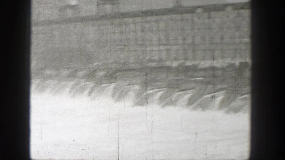 1938 Washington home-movie frame showing a dam spillway with water pouring down in a wide pale cascade.