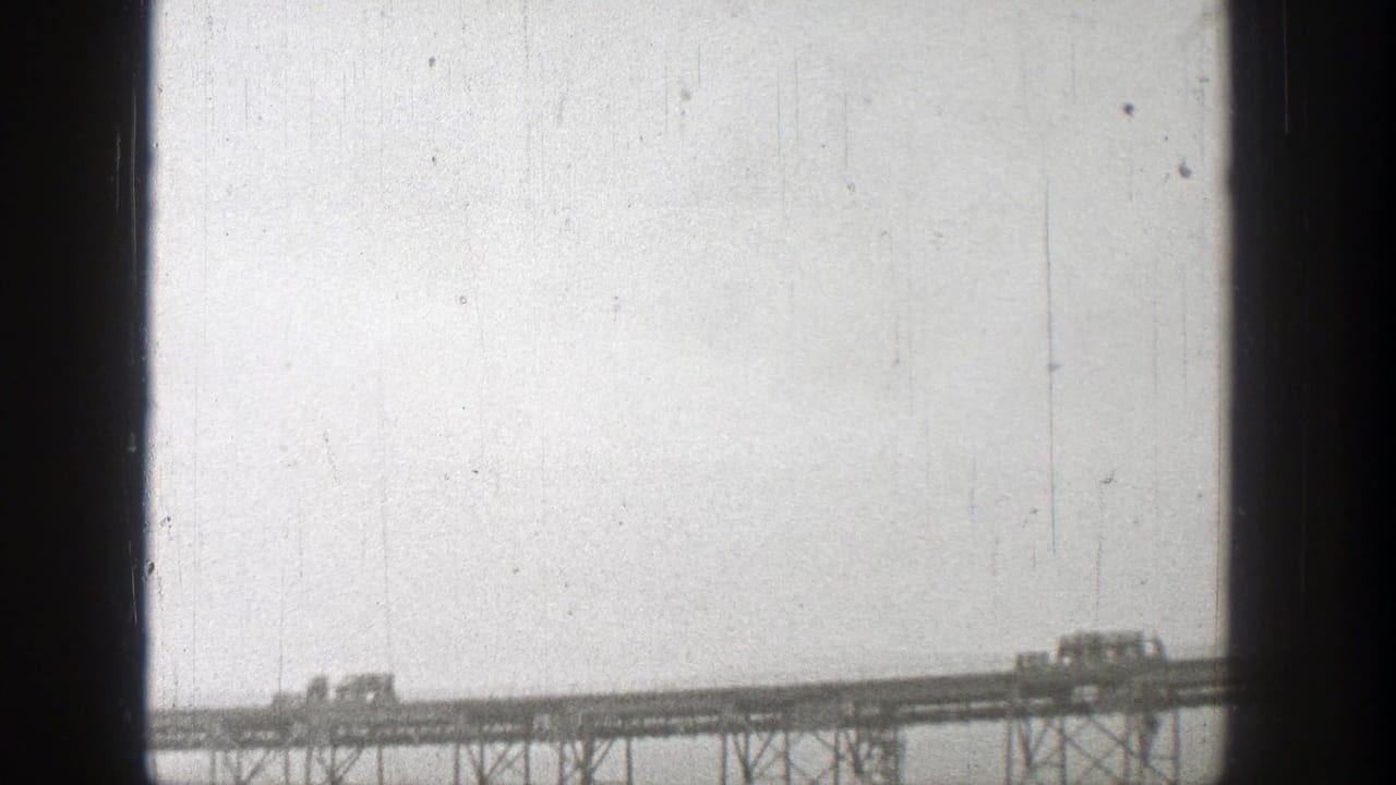 Small vehicles crossing a high steel bridge under a pale sky.