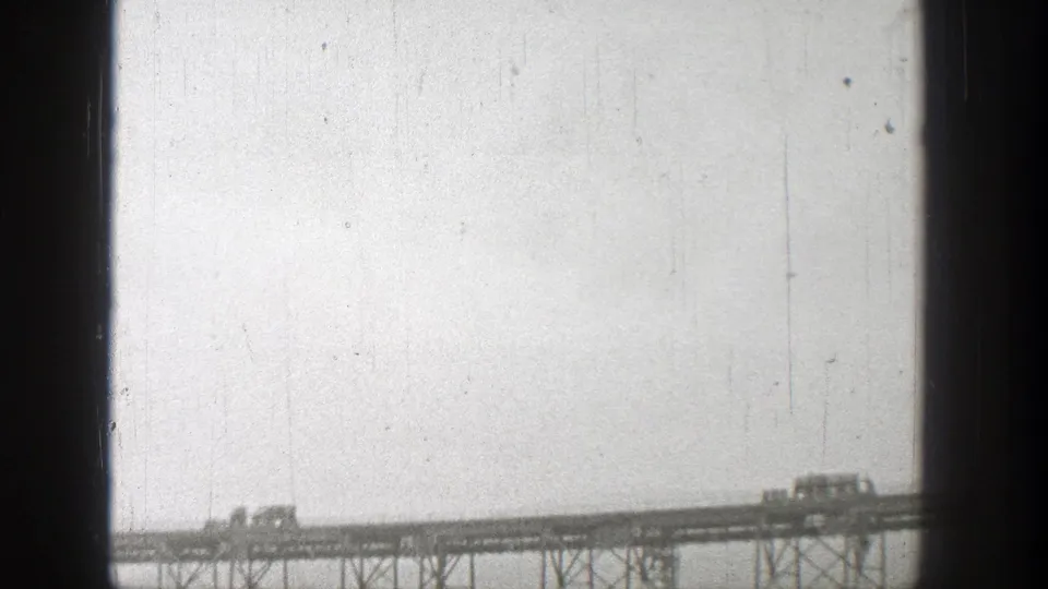 Distant 1938 Washington view of vehicles traveling across a steel truss bridge near the dam area.