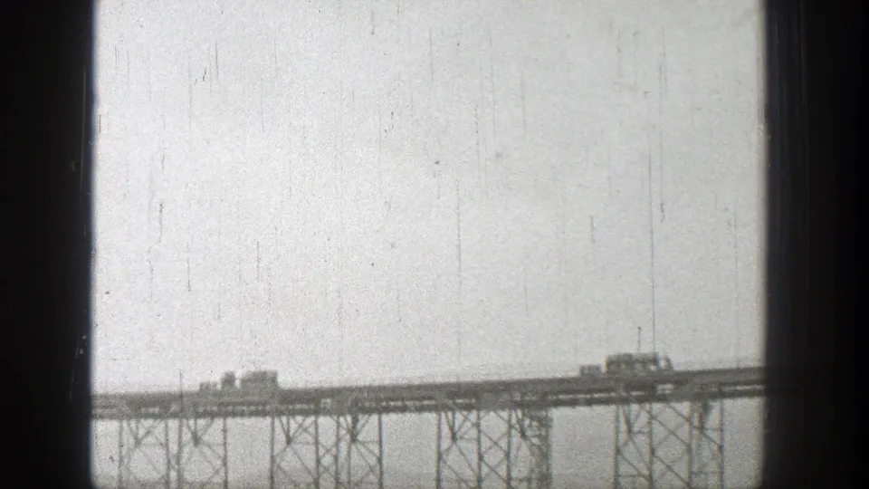Washington 1938 home-movie frame with two small vehicles on a steel truss bridge above a distant landscape.