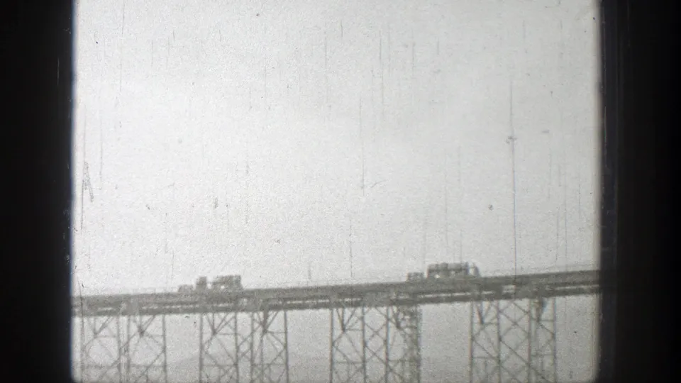 Distant Washington 1938 bridge view showing small vehicles spaced along a steel truss structure.
