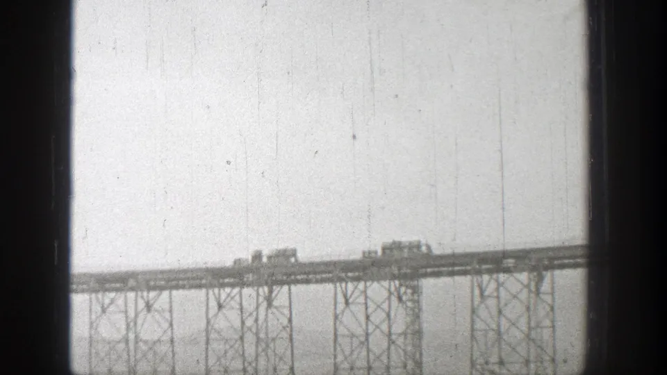 Distant 1938 Washington view of railway vehicles crossing a steel-supported bridge, partly obscured by dark vertical framing.