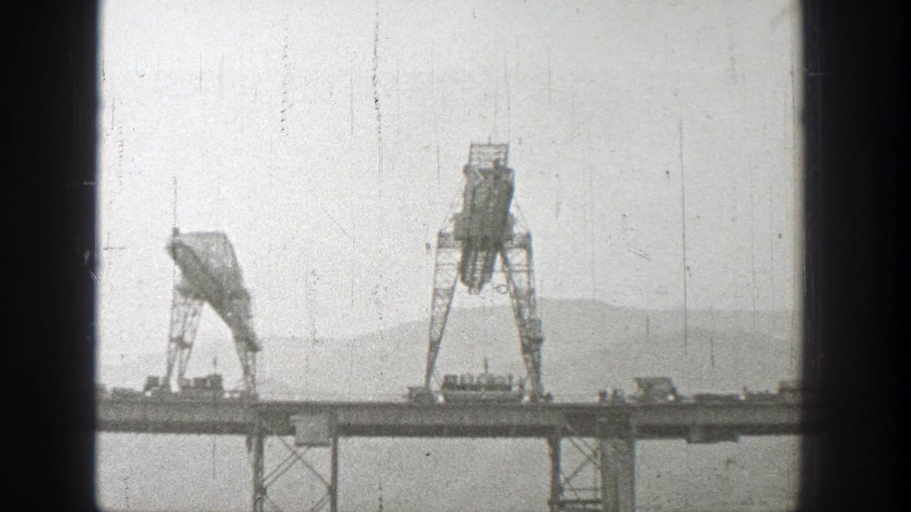 Two large cranes stand on elevated bridge construction steel over water.