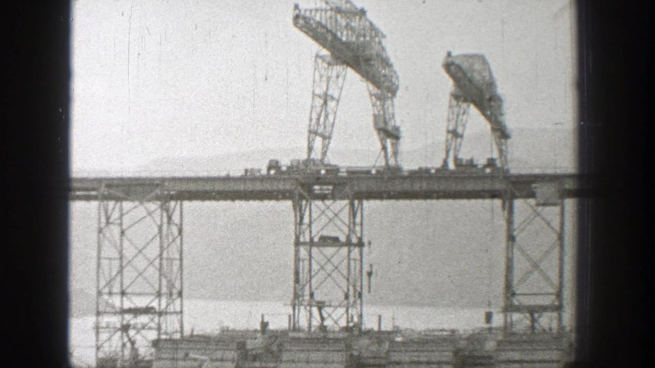 Two cranes sit on a high bridge framework above vertical support towers.