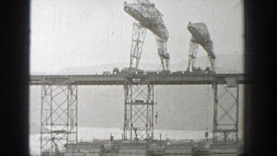 1938 Washington frame with paired gantry cranes on elevated bridge steel, seen across water through a soft 8mm scan.