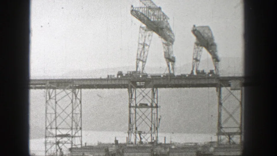 1938 Washington 8mm still showing cranes and lattice towers on a bridge construction span over water.
