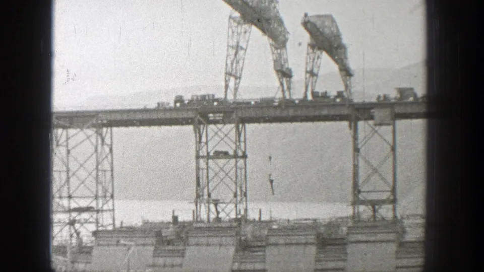 Late-1930s Washington bridge construction frame with two cranes, steel supports, and a hook lowered over the water.